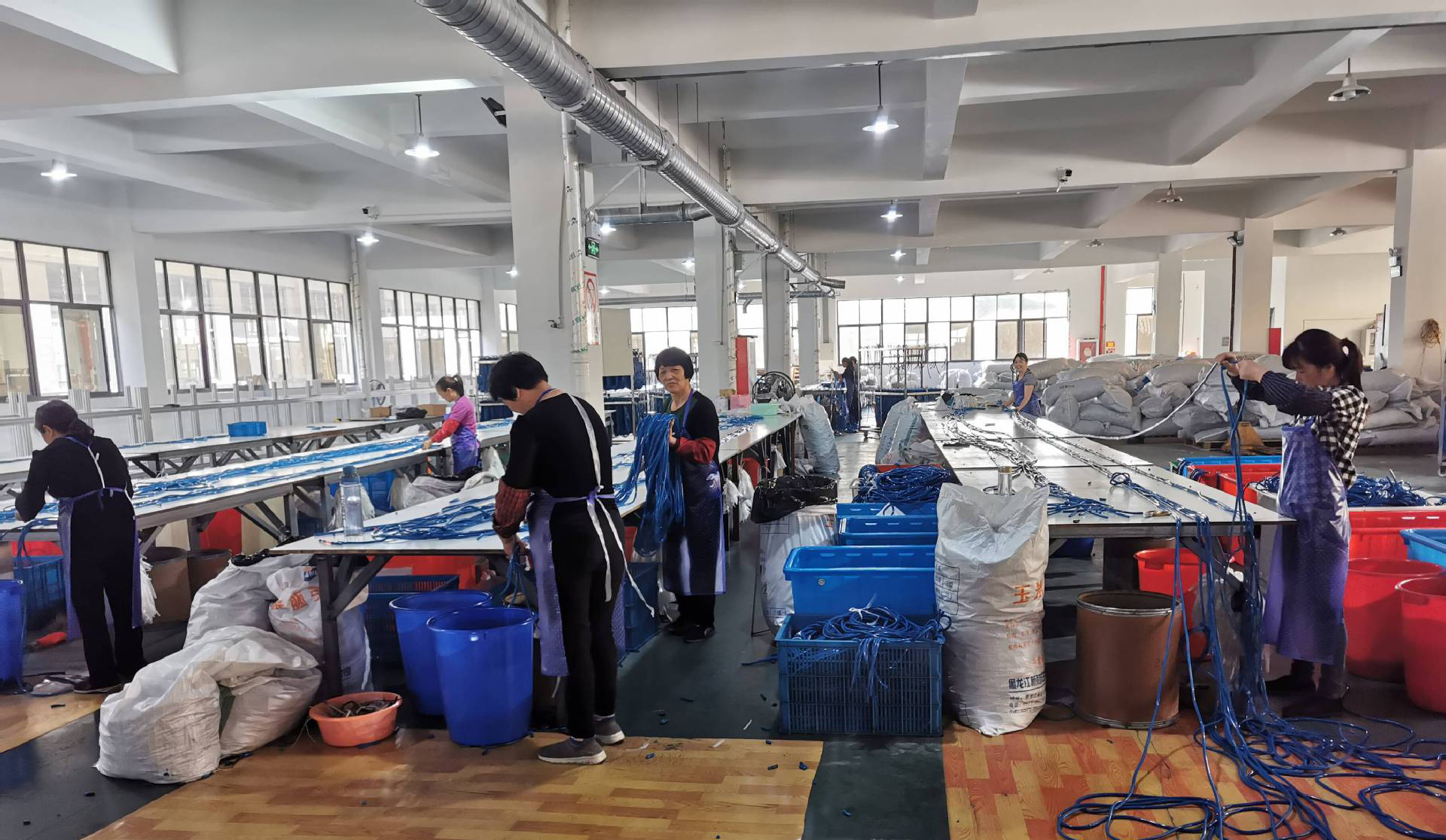 Assembly line for blue resistance bands with workers processing and packaging, showcasing large-scale and efficient production flow.